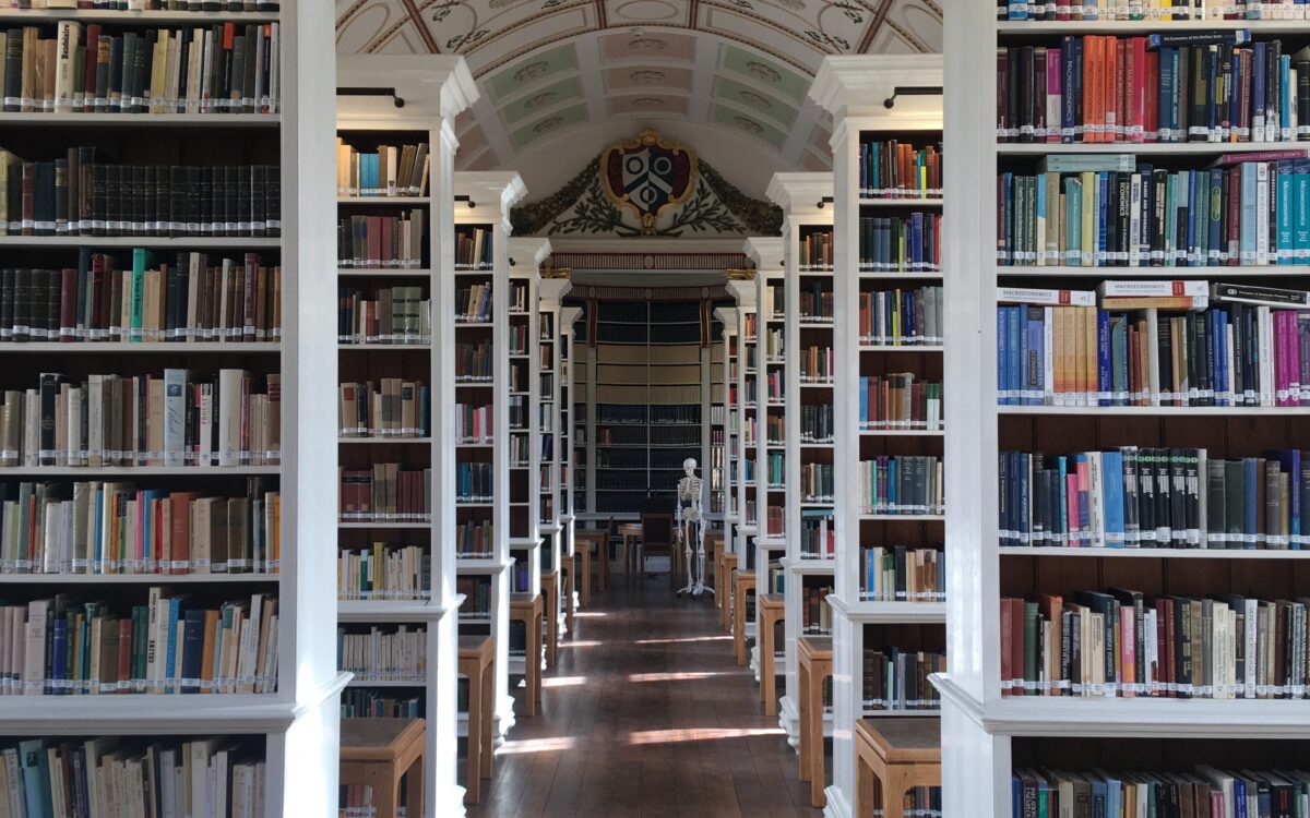 Interior of the college library with arched ceiling, tall bookshelves, wooden floors, and study desks lined along a central aisle