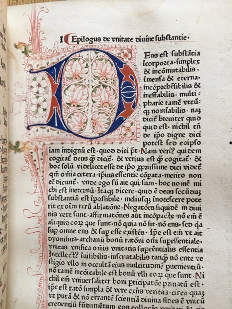 Close-up of an illuminated manuscript page featuring ornate medieval lettering and Latin text from a historical book