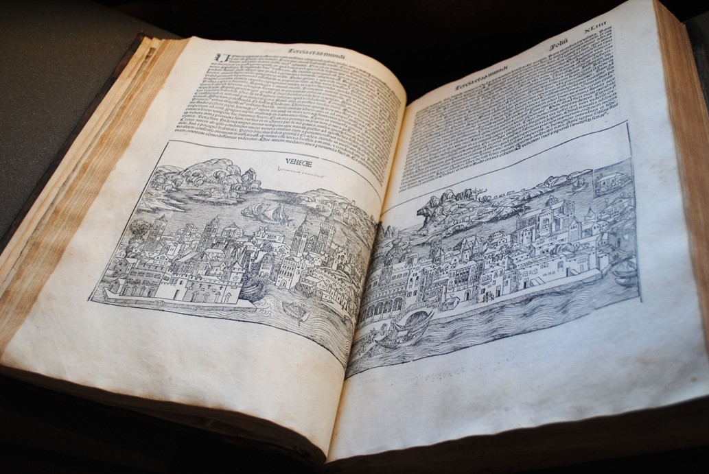 Open antique book showing a woodcut illustration of a historic cityscape with Latin text above the image