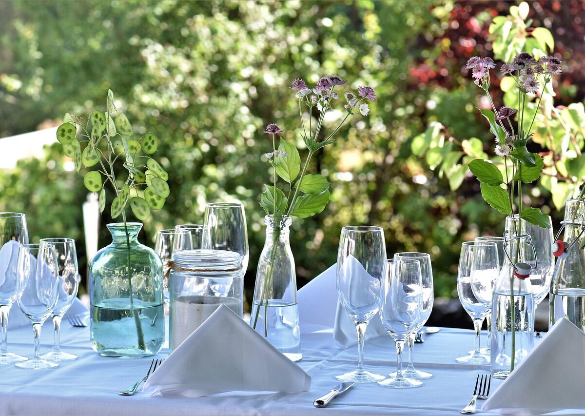 Table set outdoors for a formal meal, with glassware and greenery