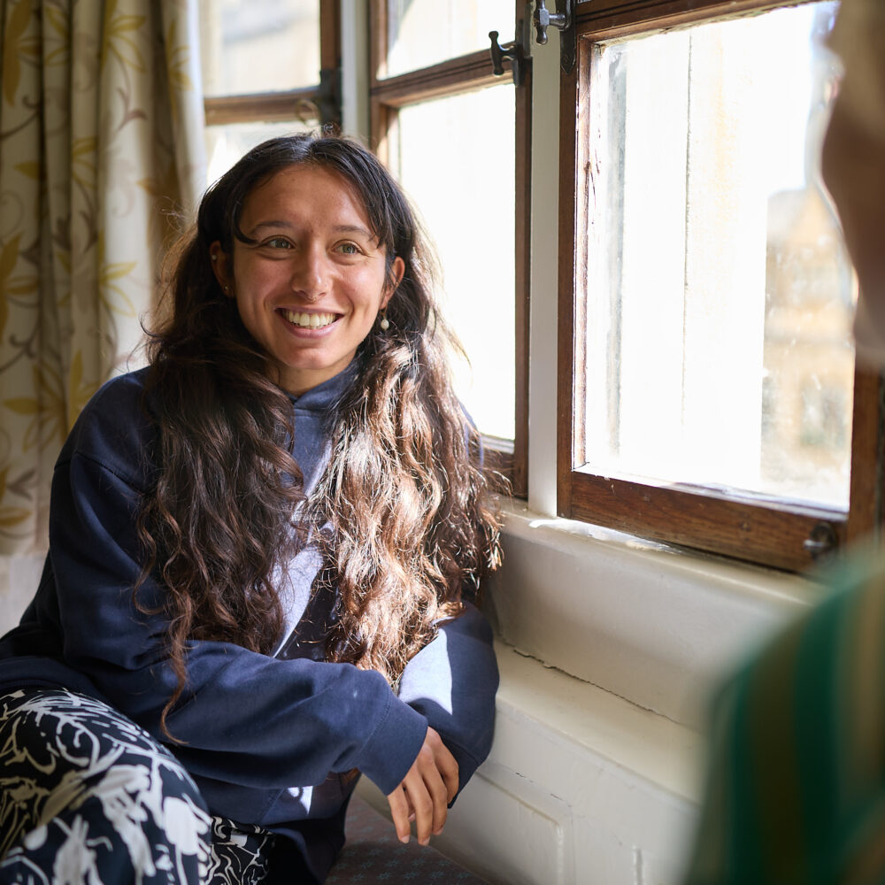 Person sitting indoors by a window, smiling