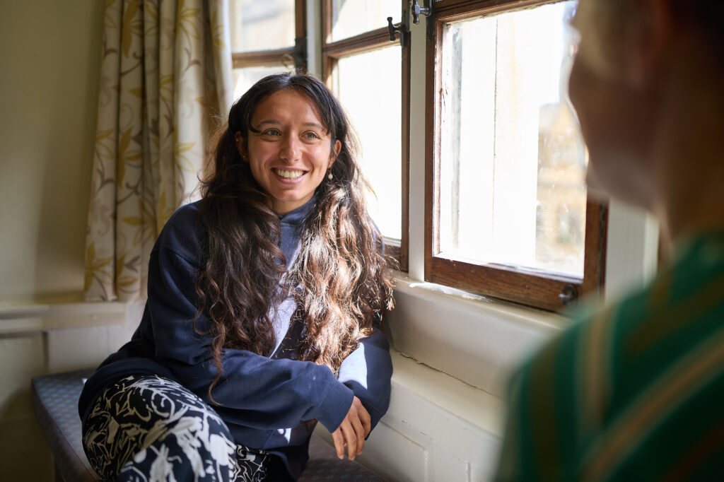 Person sitting indoors by a window, smiling