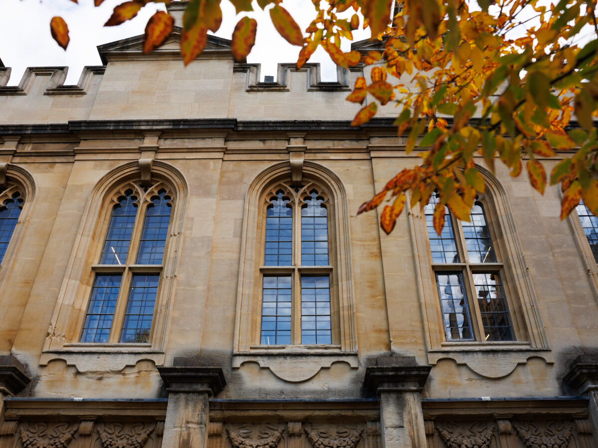 Upper section of a historic college building framed by autumn leaves