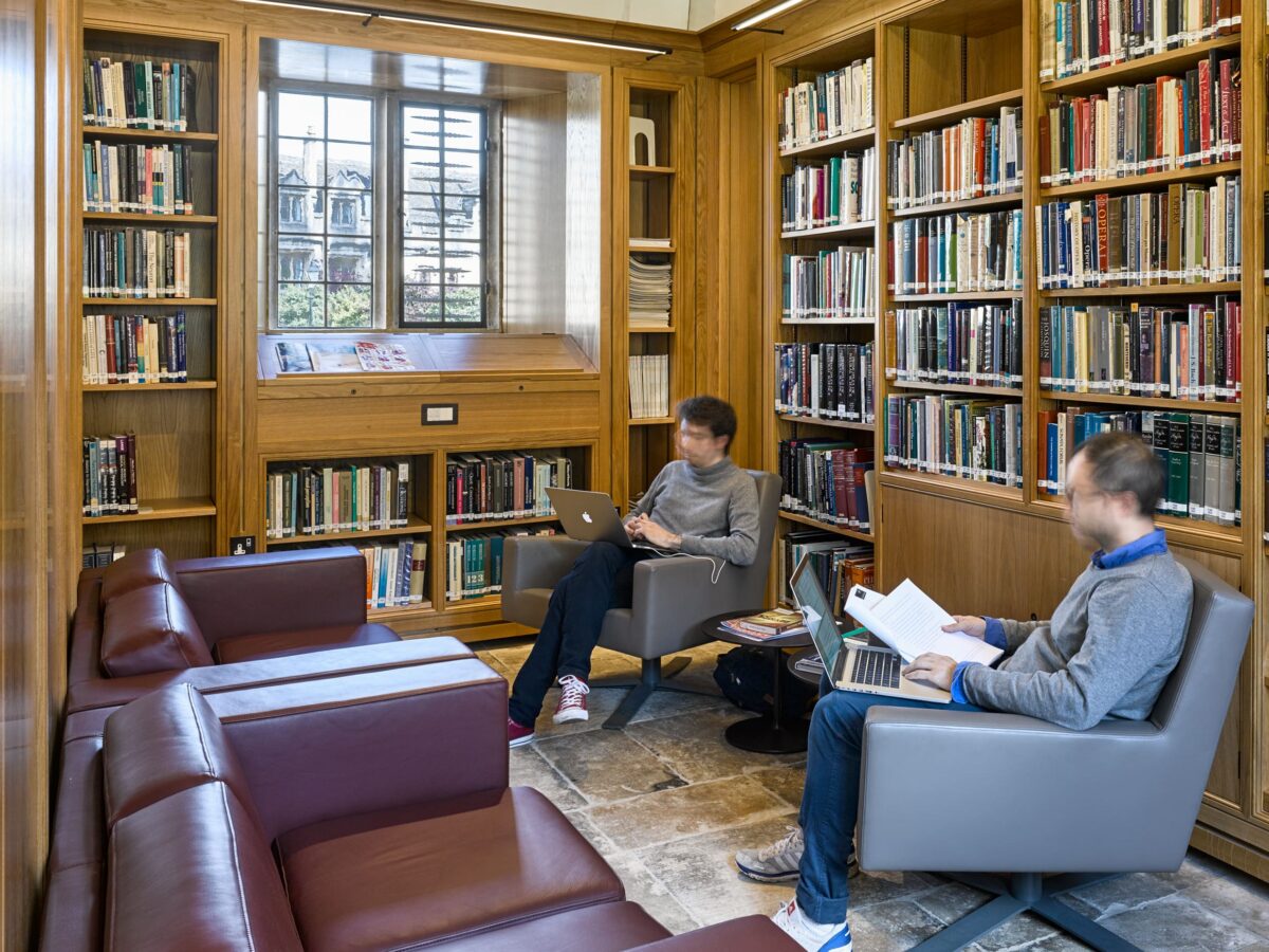 Two people in the comfy seating area in the Smith Reading Room with bookshelves and armchairs