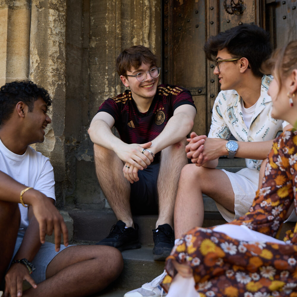 Small group of students sitting together on college building steps, engaged in conversation.