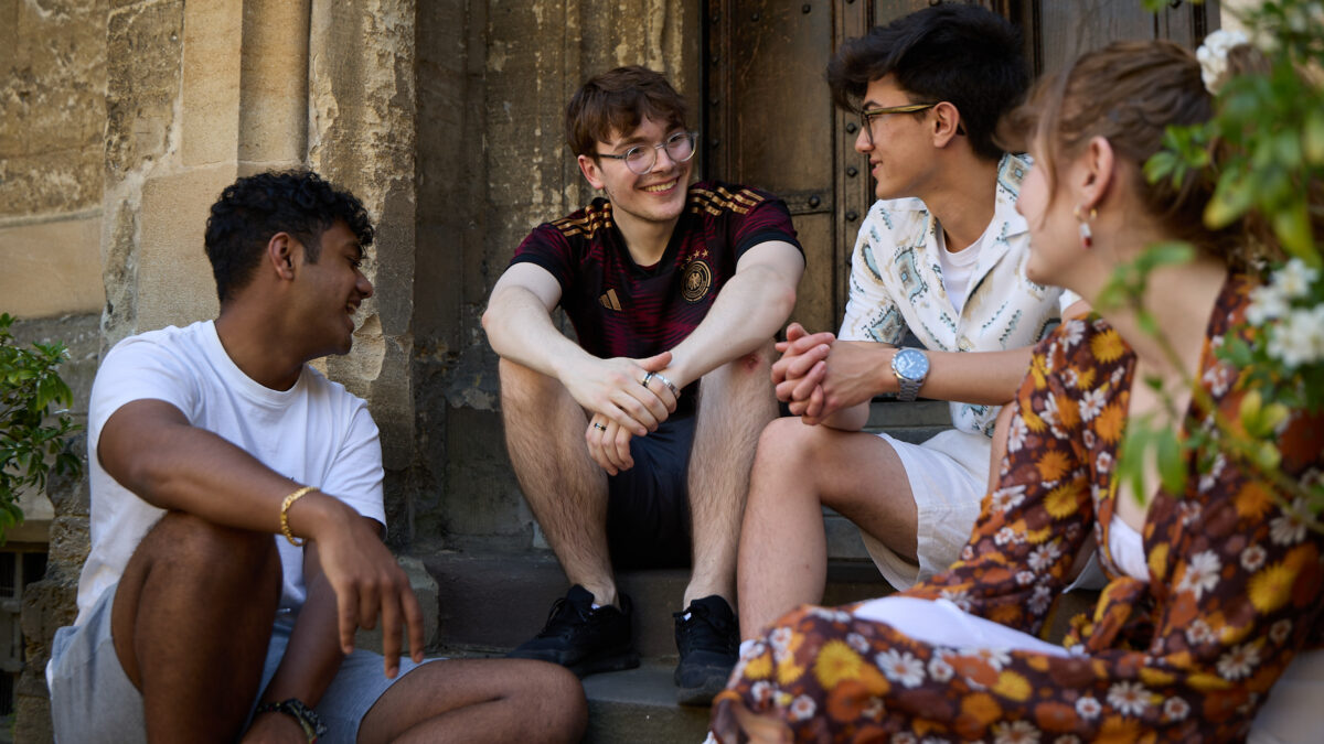 Small group of students sitting together on college building steps, engaged in conversation.