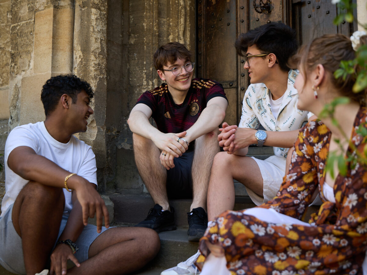 Small group of students sitting together on college building steps, engaged in conversation.