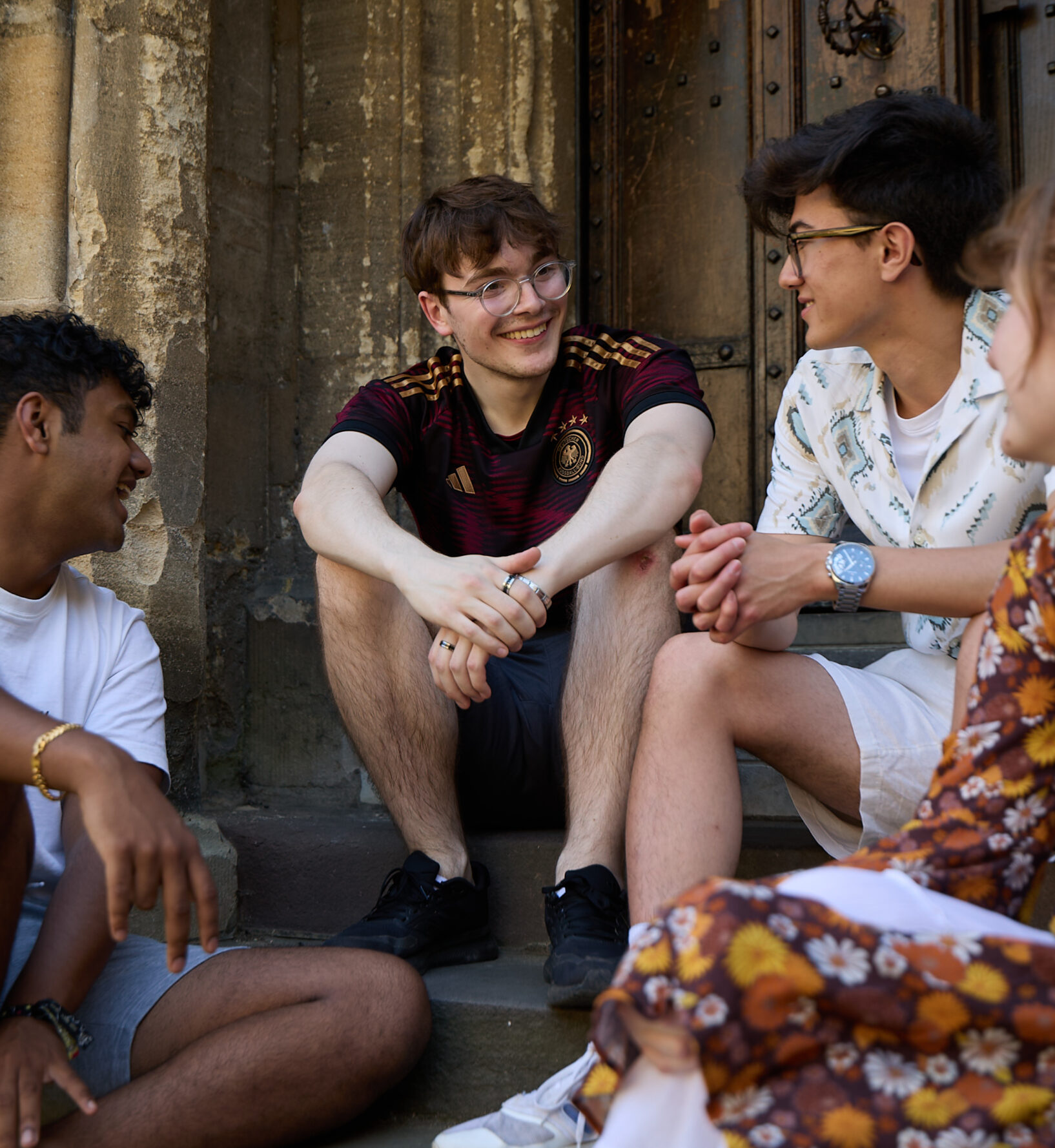 Small group of students sitting together on college building steps, engaged in conversation.