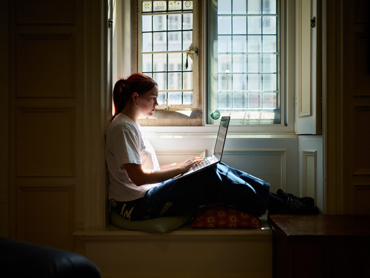 Person sitting by a window in an alcove, working on a laptop
