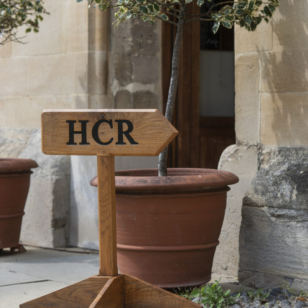 mall sign reading “HCR” placed by a plant pot beside a stone wall.