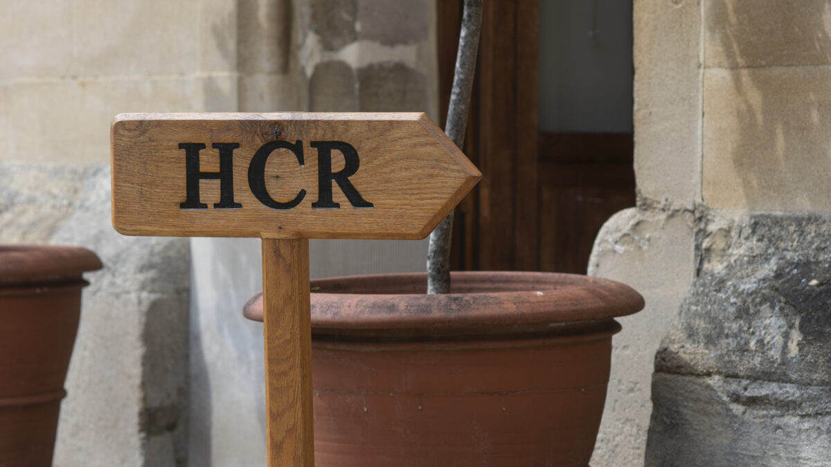 mall sign reading “HCR” placed by a plant pot beside a stone wall.