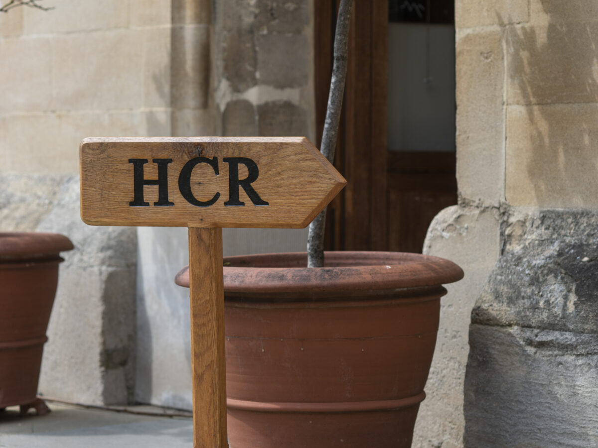 mall sign reading “HCR” placed by a plant pot beside a stone wall.