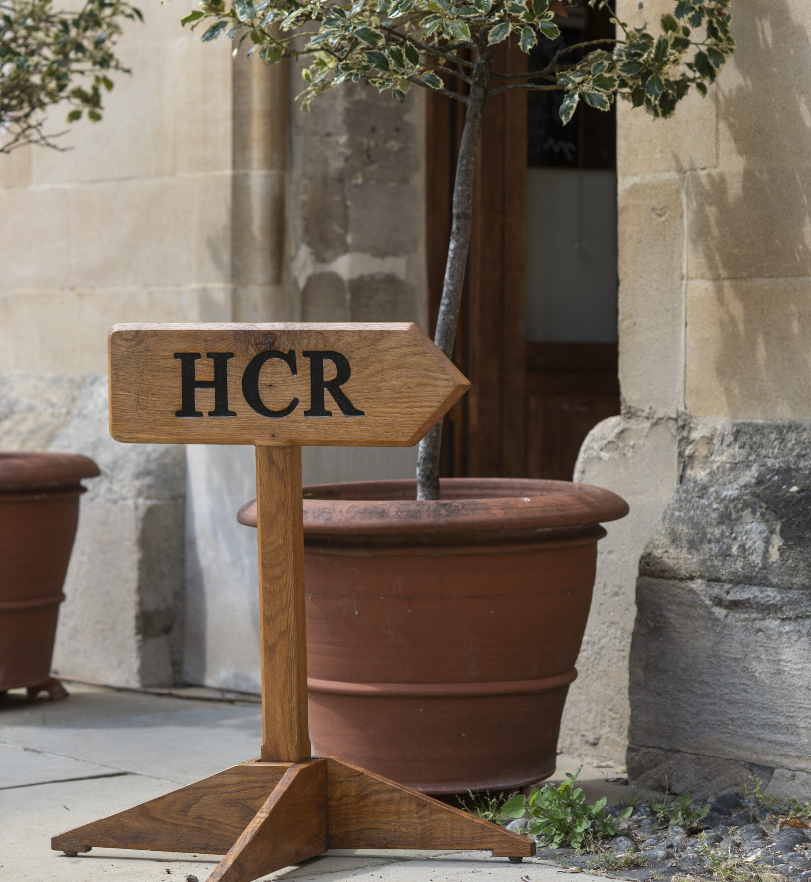 mall sign reading “HCR” placed by a plant pot beside a stone wall.