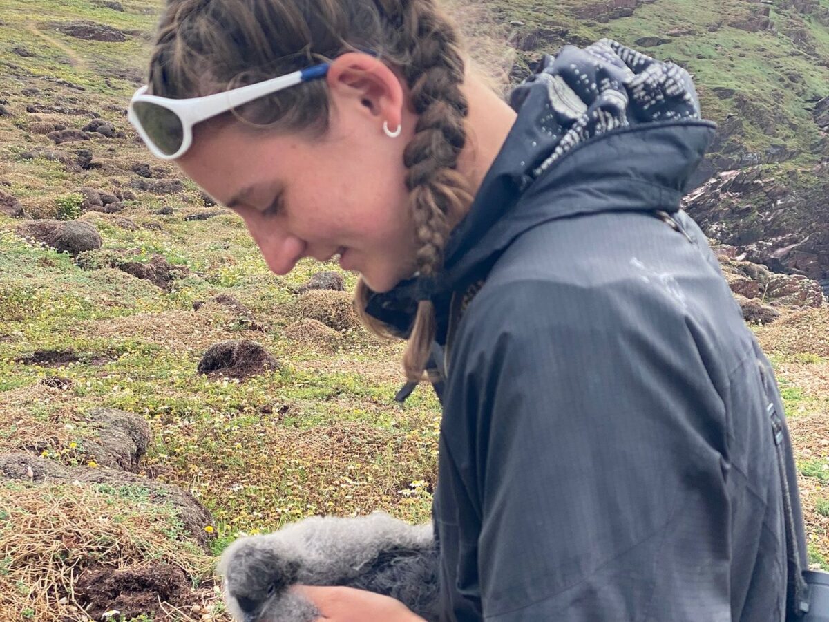 Student outdoors examining a bird in a grassy area