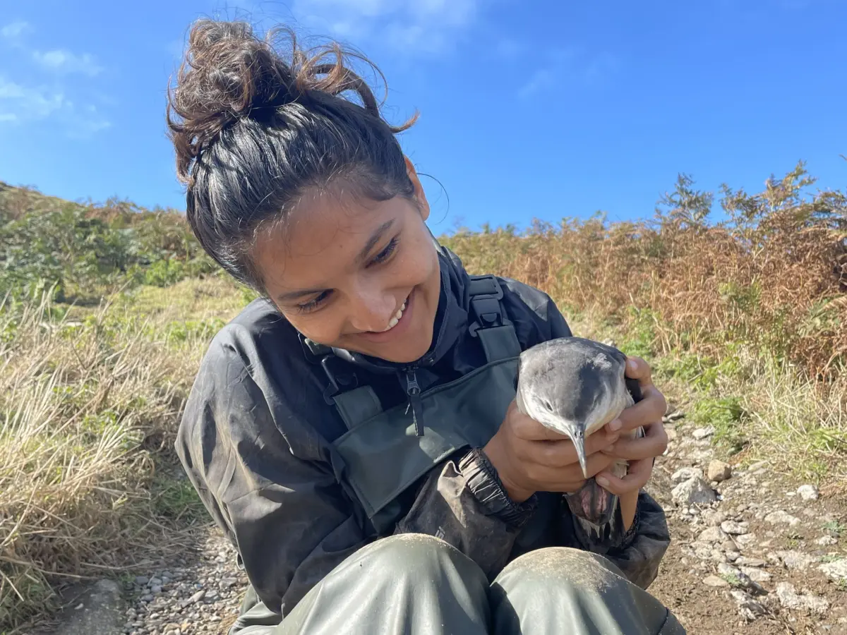 Student outdoors examining a bird in a grassy area
