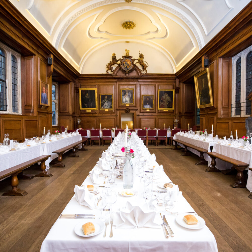 The Hall at Brasenose College laid up for dinner with white table clothes, cutlery, crockery, flowers and bread rolls.