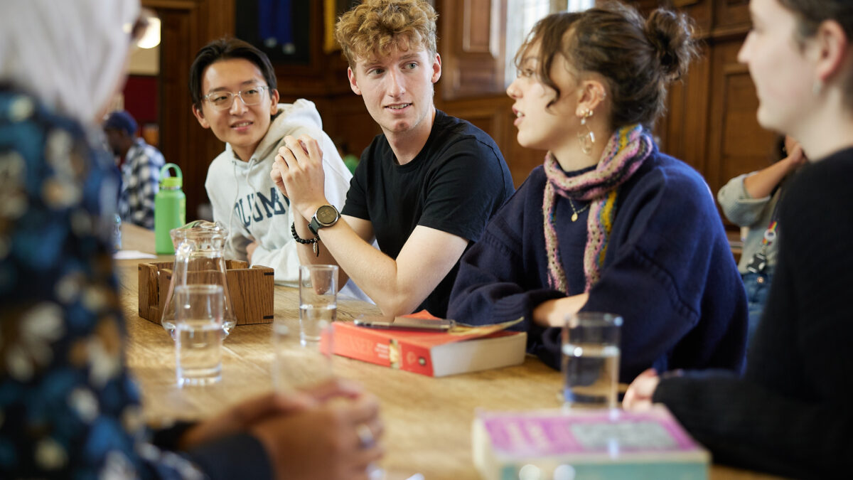 Small group of people sitting around a table indoors, talking with books in front of them