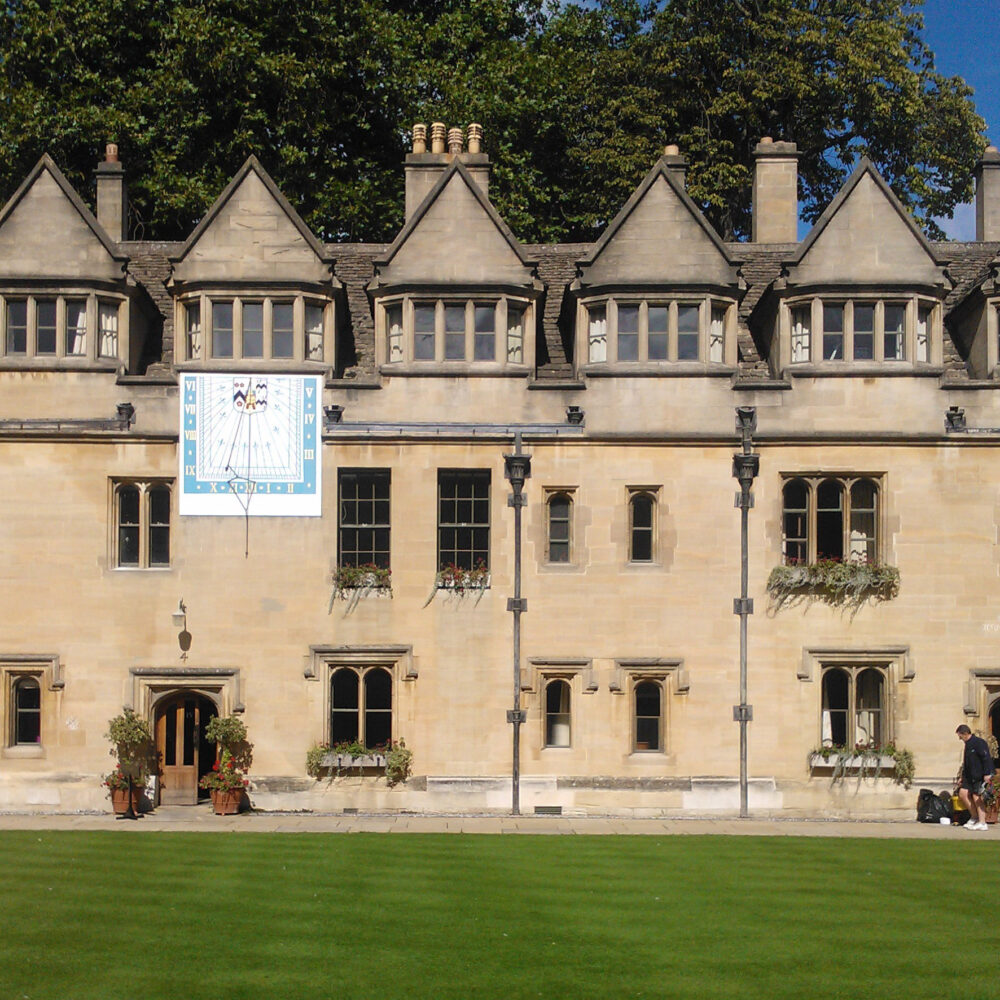 Exterior view of a historic college building facing a lawn with a sundial mounted on the side of the building