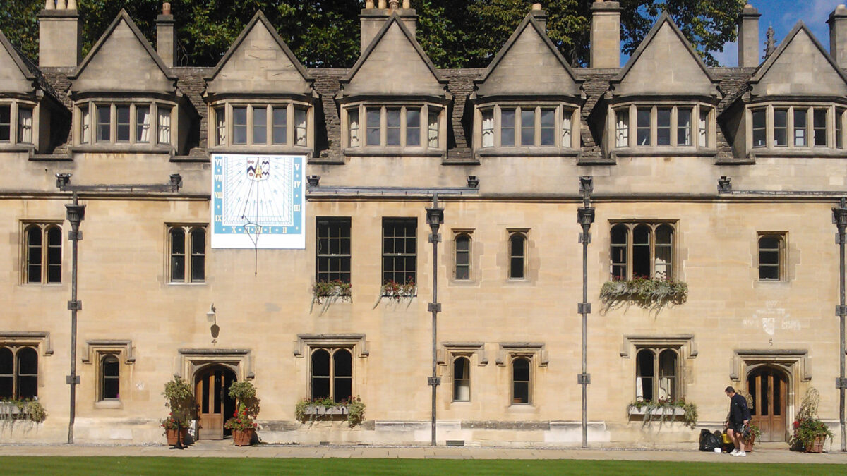 Exterior view of a historic college building facing a lawn with a sundial mounted on the side of the building