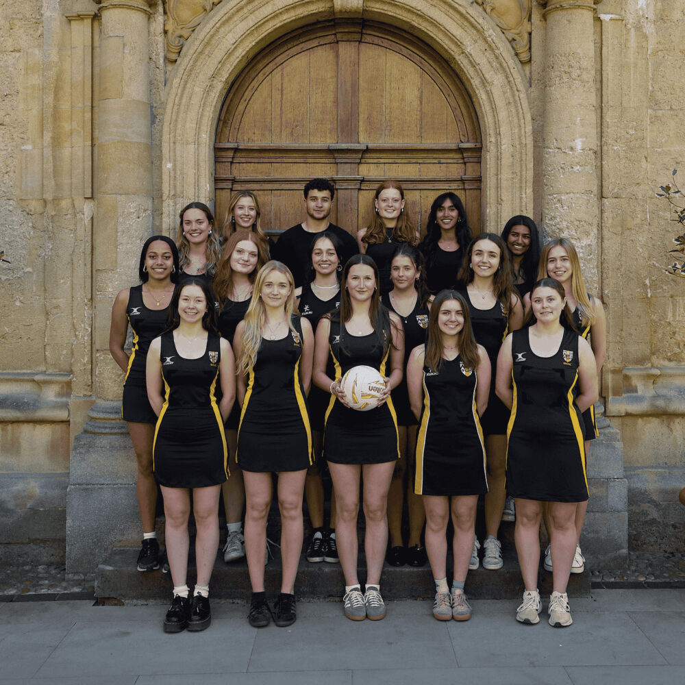 College netball team standing outdoors in team kit, posing for a group photo.