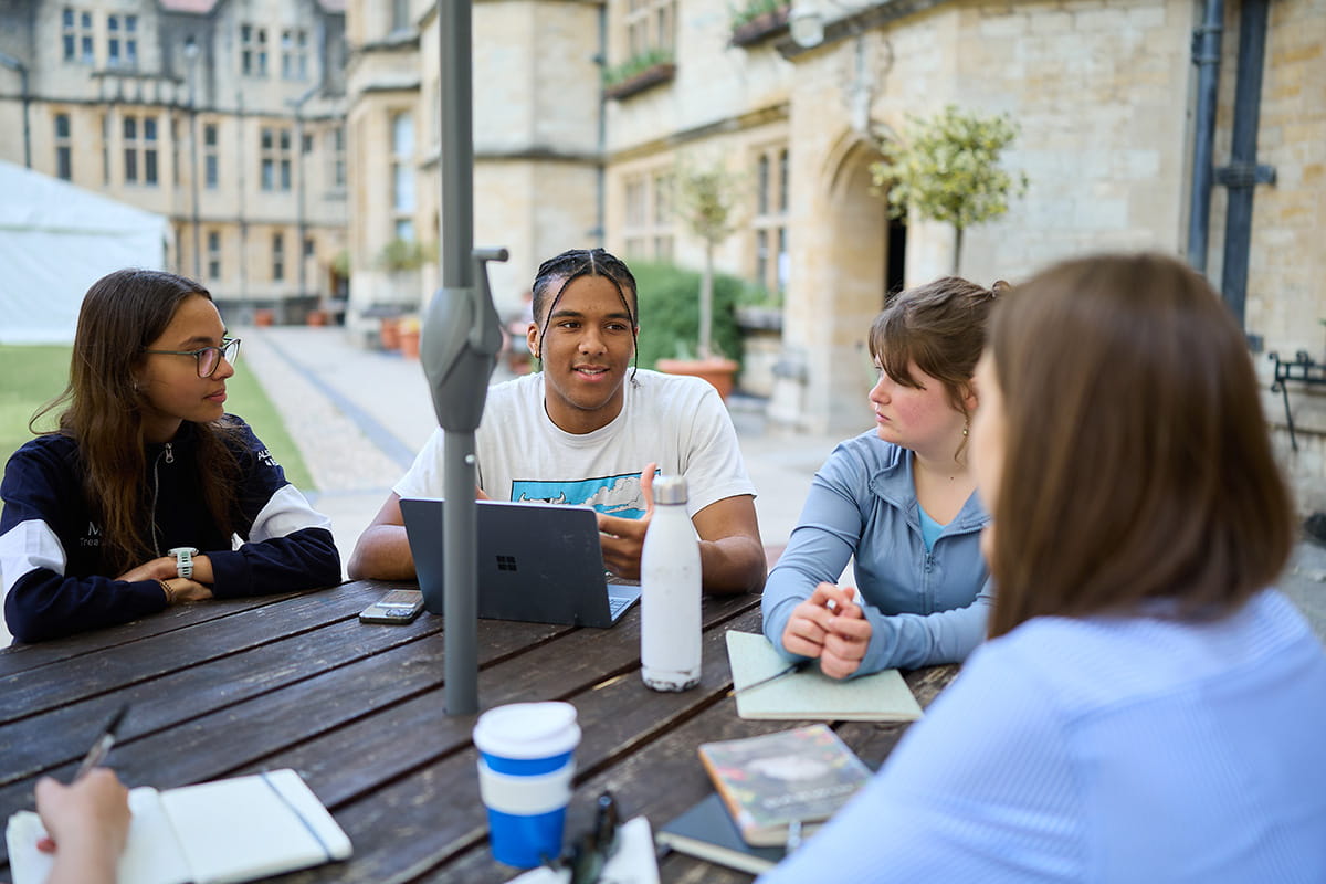 Students sitting together at an outdoor table in the quad taking part in a tutorial