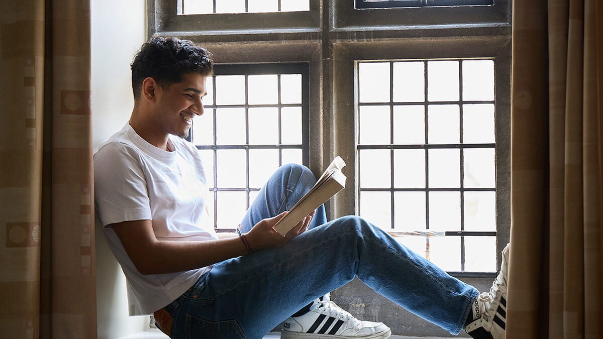 Student sitting in a window alcove reading a book in a college room
