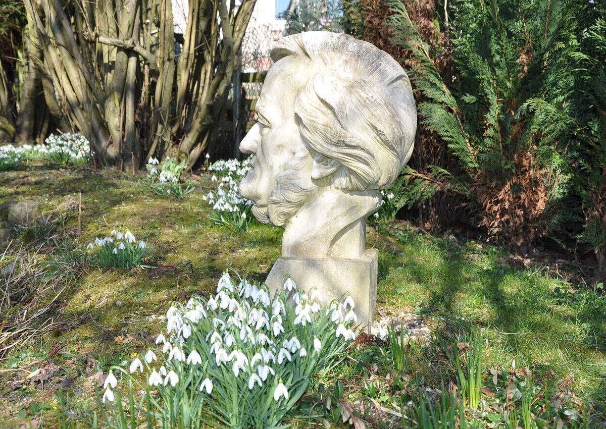 Stone sculpture of a head displayed outdoors among snowdrops