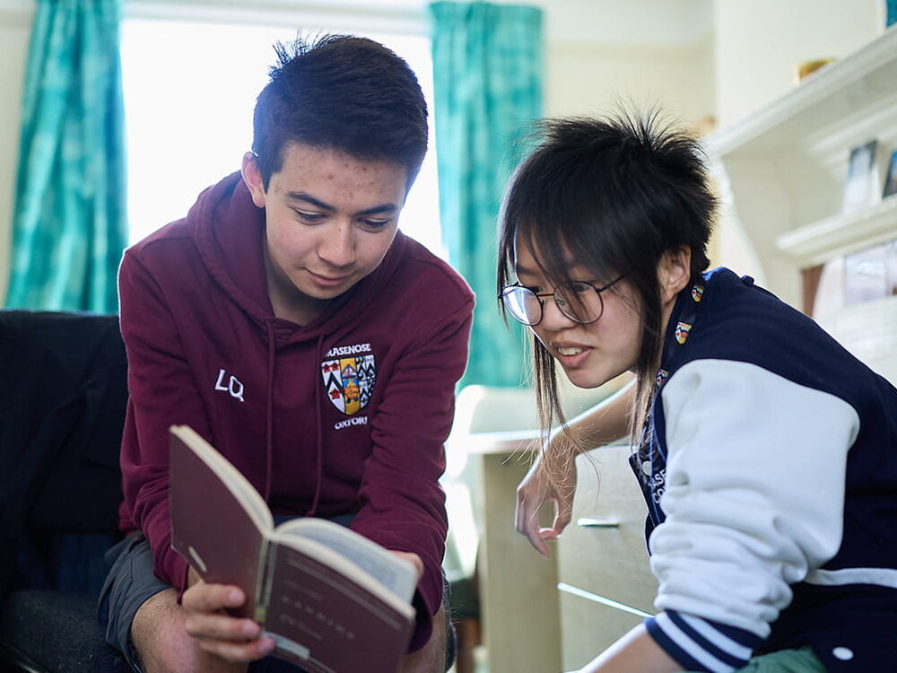 Two students reading and discussing a book together in a college room
