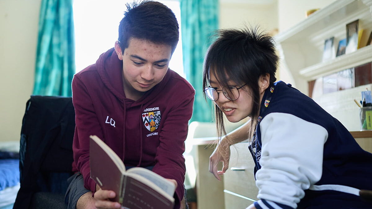 Two students reading and discussing a book together in a college room