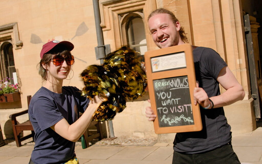Student volunteers welcoming visitors, holding a sign reading ‘Brasenose – you want to visit here