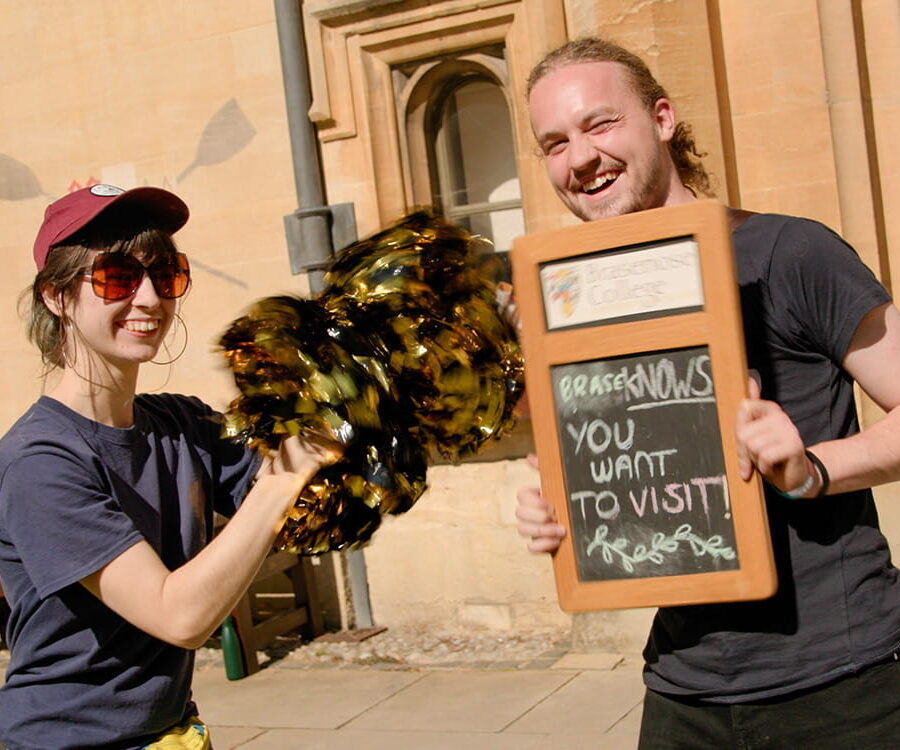 Student volunteers welcoming visitors, holding a sign reading ‘Brasenose – you want to visit here