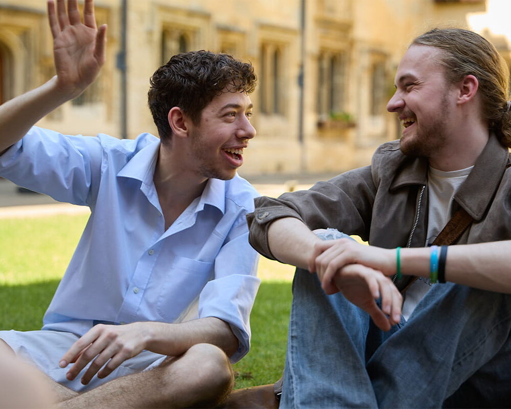 Two people sitting outdoors, talking and smiling in the college quad