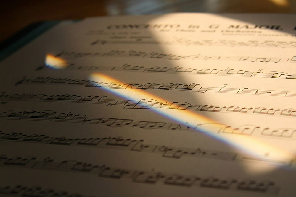 Close-up of printed sheet music illuminated by sunlight, with a soft rainbow of light falling across the page