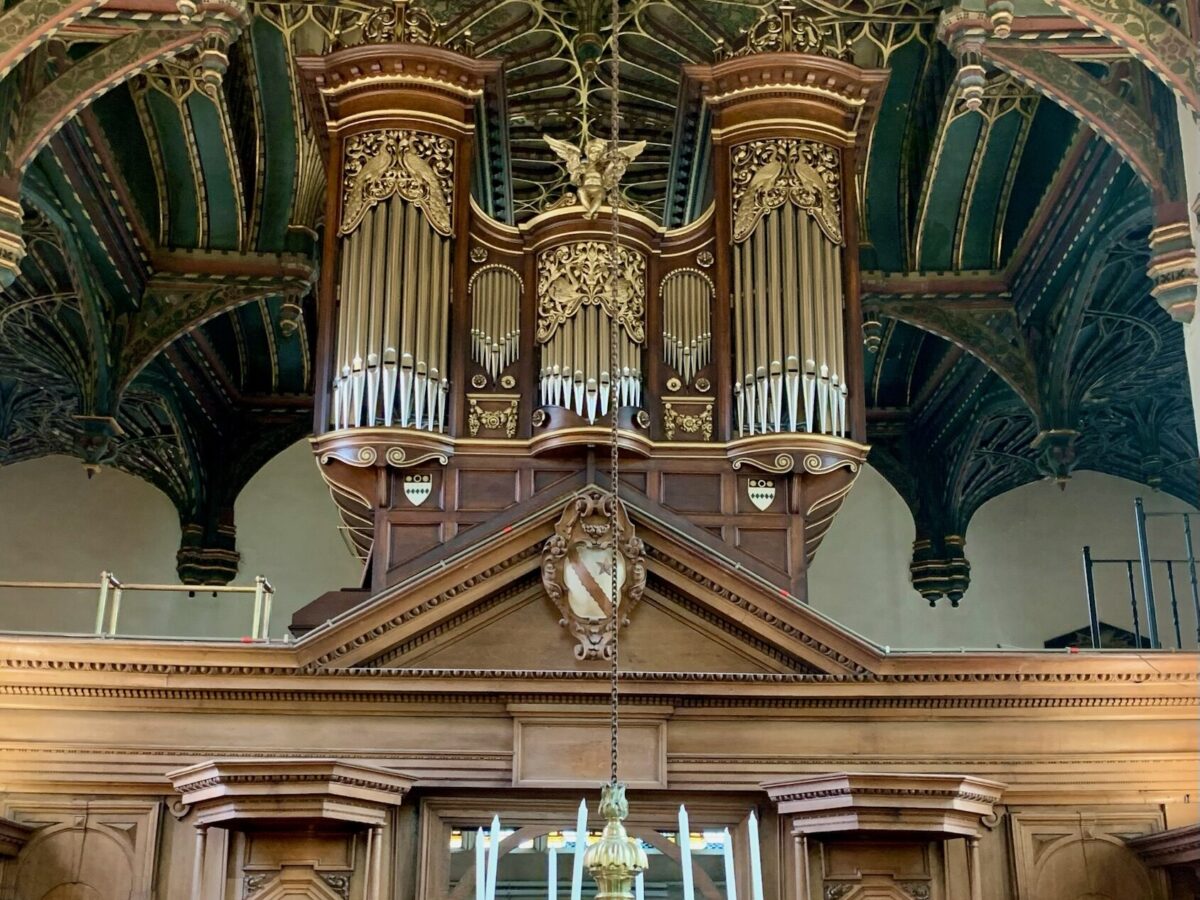 The chapel organ set beneath a richly decorated vaulted ceiling, with wooden panelling and candlelight below.