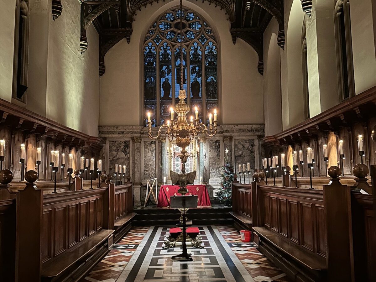 View down the chapel towards the altar, with wooden stalls, candlelight, and the vaulted ceiling.