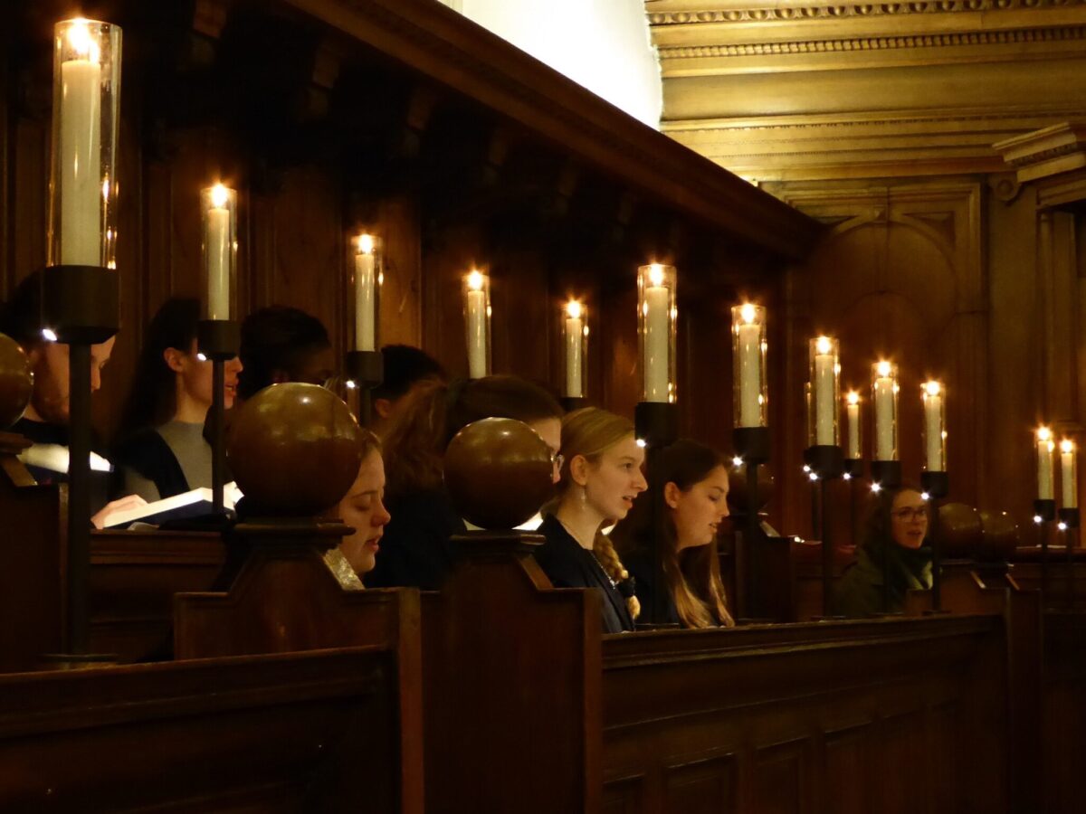 College choir singing in candlelit chapel stalls during a service.