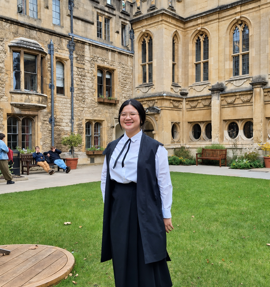 Scholarship student Belinda standing in Deer Park in her gown, with a view behind of the library and the Radcliffe Camera.