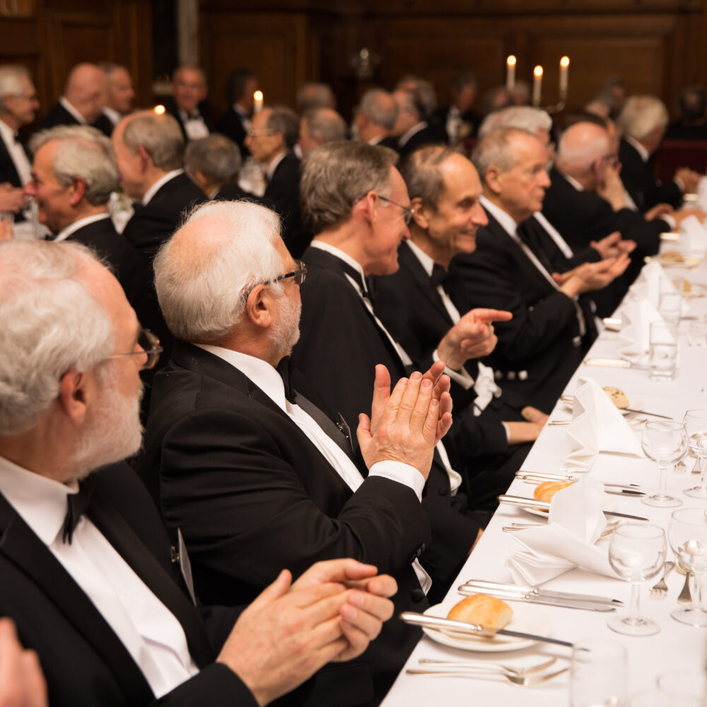 Grey haired men wearing black tie sat at a Gaudy dinner in the Hall