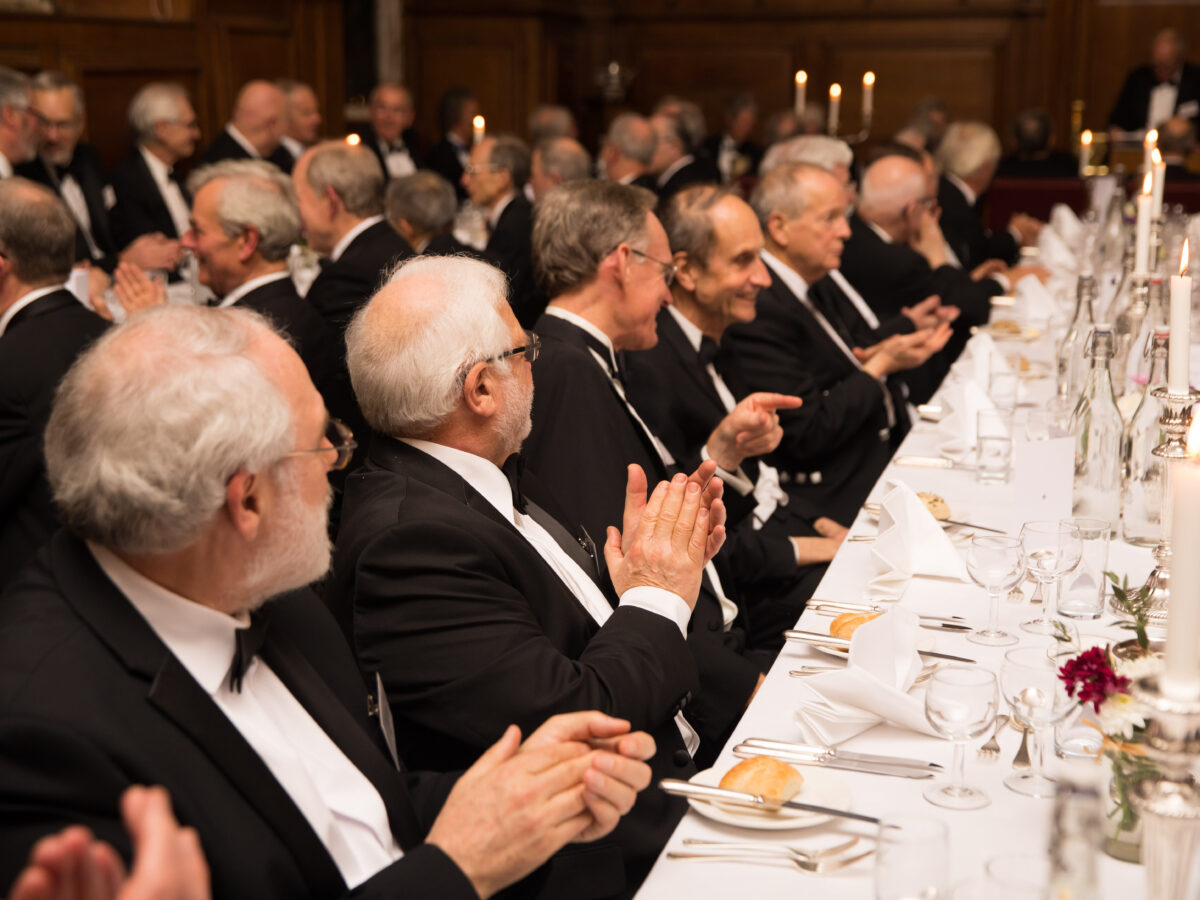 Grey haired men wearing black tie sat at a Gaudy dinner in the Hall